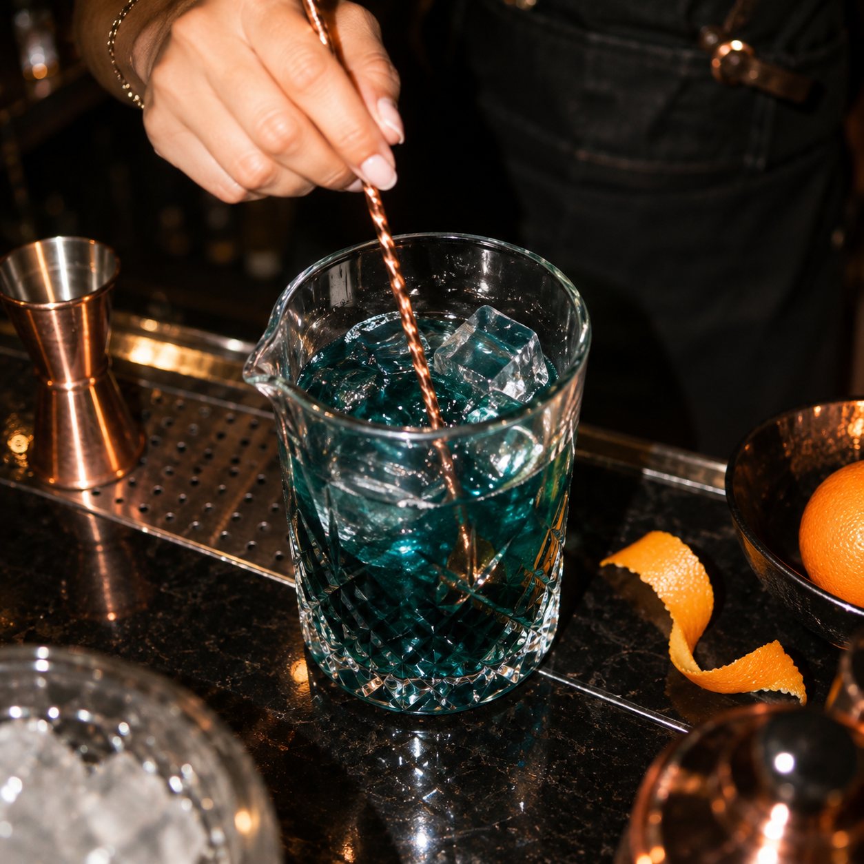 Bartender stirring a teal craft cocktail with a copper bar spoon